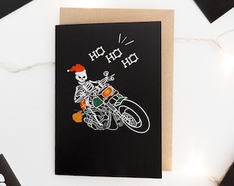 May include: A black Christmas card with a white skeleton riding a motorcycle. The skeleton is wearing a Santa hat and holding a gift. The card says "Ho Ho Ho" in white text.