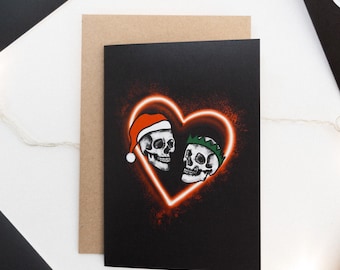 May include: A black Christmas card with two skulls in a neon heart. The skull on the left is wearing a Santa hat and the skull on the right is wearing a green elf hat.