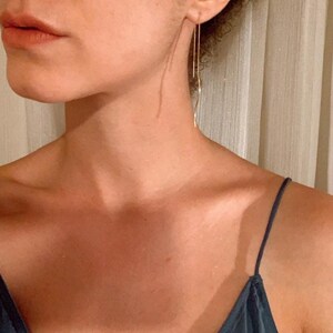 Puede incluir: Primer plano del pecho y los hombros de una persona que lleva un top azul oscuro con tirantes finos. La persona tiene el pelo largo y oscuro y lleva pendientes de oro delicados.