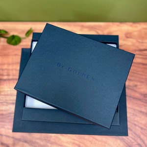 May include: A stack of three dark blue boxes with the text "BE.GOLDEN" printed on the top box.