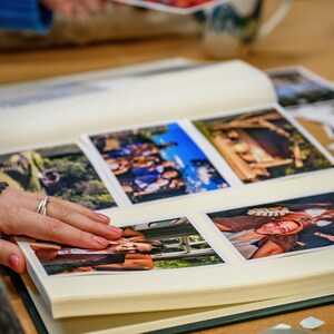 An album full of photos lies open on a table and someone is flicking through it. All the photos in the album look really colourful and fun.