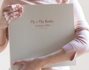 May include: A white wedding album with the text "Mr & Mrs Barker, Lartington Hall, 12th January 2019" printed in rose gold.