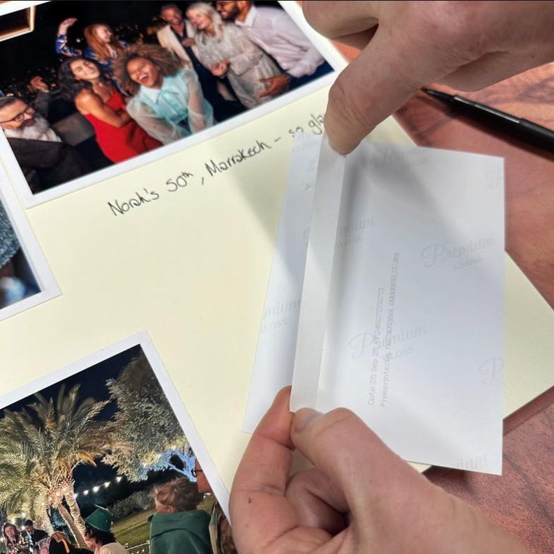 A piece of double-sided mounting tape is being applied to the back of a photo before being stuck into an open photo album.