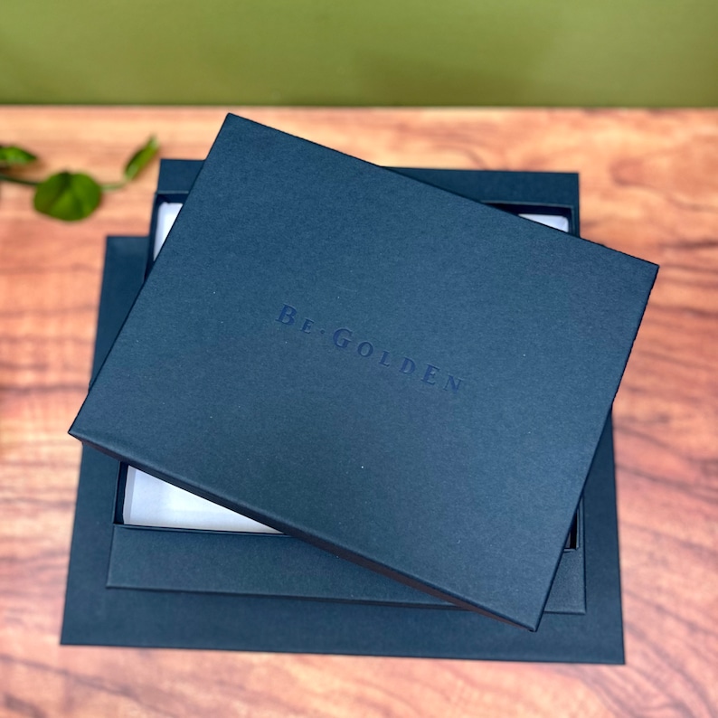 on a table you have a small pile of navy blue presentation boxes. These are designed for the large leather photo album and are branded with begolden