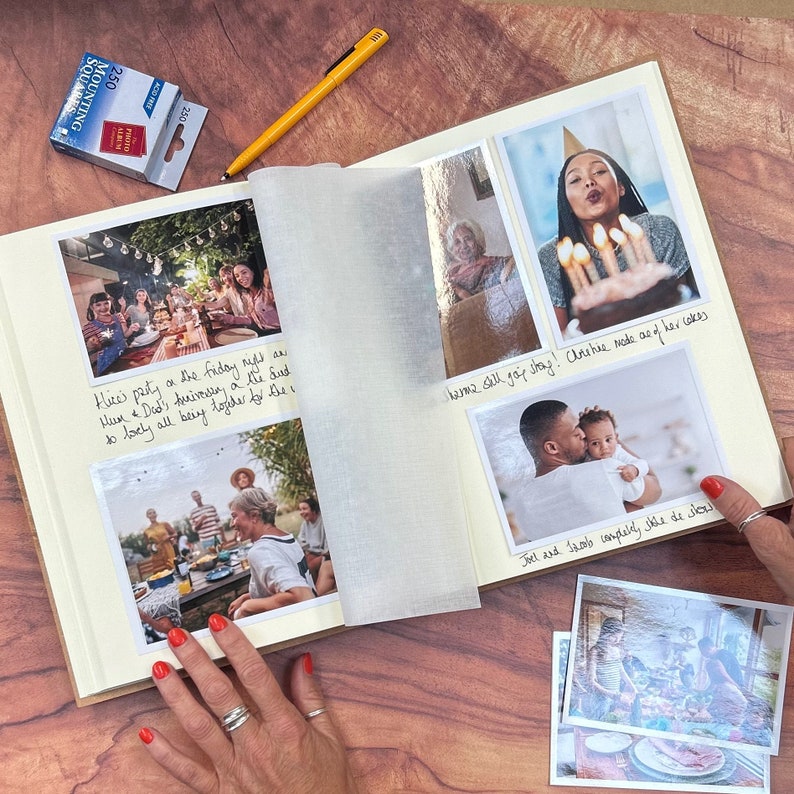 there is an A4 photo album on a table. It is full of 4"x6" family photos. The woman is putting photos into the photo album with mounting squares