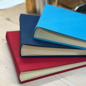 On a table there are three linen photo albums in various colours, all stacked up on top of each other. Red on the bottom, then navy blue and then a mid sky blue on the top.