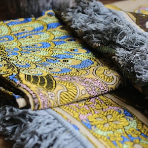 May include: Two decorative throw pillows with fringed edges. The pillows feature a floral pattern with yellow, blue, and pink accents. The pattern on one pillow is a peacock design.