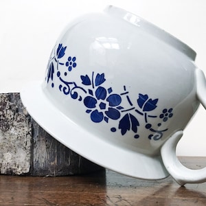 Könnte beinhalten: Weiße Keramik-Toilette mit blauem Blumendesign. Die Toilette hat einen Griff und steht auf einer Holzoberfläche.