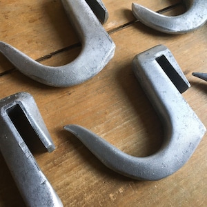 Könnte beinhalten: Ein Satz von fünf silbernen Metallhaken mit einem einzigartigen, gebogenen Design. Die Haken sind aus strapazierfähigem Metall gefertigt und haben eine glatte, polierte Oberfläche.
