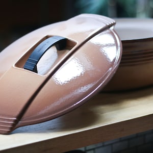 Puede incluir: Una cacerola de cerámica ovalada marrón con tapa. La tapa tiene una manija negra y el texto "Le Creuset" es visible en la tapa.