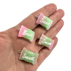 May include: Four pink and green candy bag charms with silver jump rings. Each charm has the word "Sweet" written in white on the front.