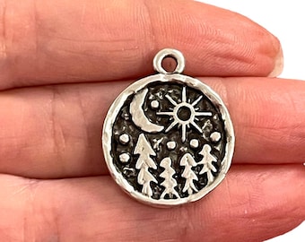 May include: Silver charm featuring a moon, sun, and pine tree design. The charm is round and has a textured surface.