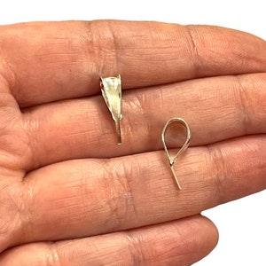 May include: Two silver pendant bails, one with a pointed end and the other with a loop, are shown in a hand.