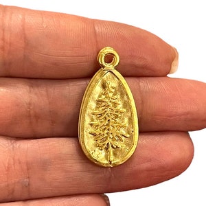 May include: Gold-toned pendant charm in the shape of a teardrop with a raised image of a pine tree inside.