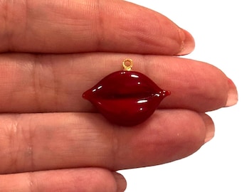 May include: A red glass charm in the shape of lips with a gold loop for hanging.