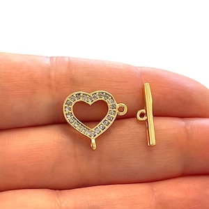 Puede incluir: Cierre de palanca en forma de corazón dorado con detalles de cristal transparente. El cierre está hecho de metal y tiene un acabado pulido.