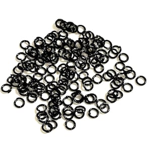 Puede incluir: Un montón grande de anillos de salto negros. Los anillos son pequeños y redondos, y todos están hechos de metal.