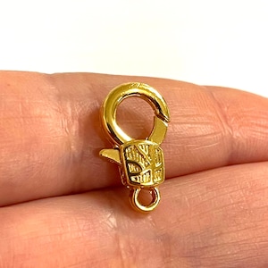 May include: Gold-toned metal lobster clasp with a decorative design. The clasp is about 1 inch long.