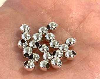 Può includere: Un mucchio di perline di metallo color argento con un foro al centro di ogni perlina. Le perline sono rotonde e lisce.