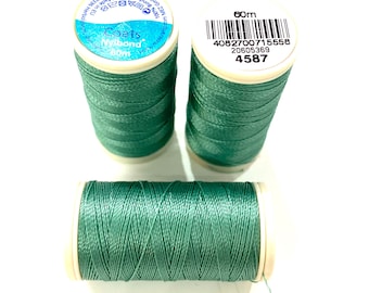 Op de afbeelding: Drie spoelen groen garen op een witte ondergrond. Het garen is gewikkeld rond witte spoelen. De etiketten luiden "Coats Nylbond 60m" en bevatten een streepjescode en andere details. Elke spoel bevat 60m garen.