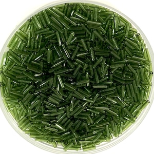 Könnte beinhalten: Nahaufnahme einer Schale gefüllt mit kleinen, dunkelgrünen Glasperlen. Die Perlen sind zylindrisch geformt und haben eine glatte, glänzende Oberfläche.