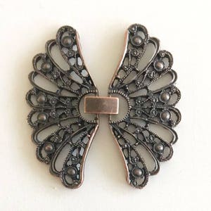 May include: Two antique-style metal clasps in the shape of a fan. The clasps are a dark bronze color and have a delicate, intricate design.