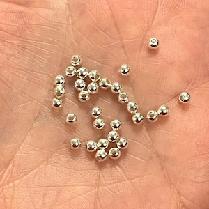 May include: A close-up of a hand holding a pile of small, silver-coloured beads.
