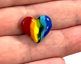 May include: A small, rainbow-colored glass heart. The heart is made of clear glass with swirls of red, orange, yellow, green, blue, and purple.