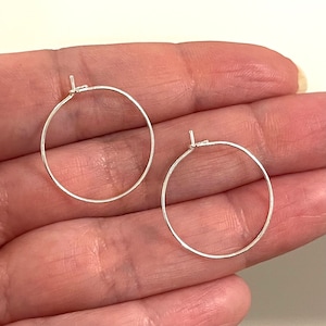 May include: Two small, silver hoop earrings. The earrings are simple, round, and have a thin profile. The hoops are shown against a light background, highlighting their metallic shine. The earrings are a classic jewellery item.