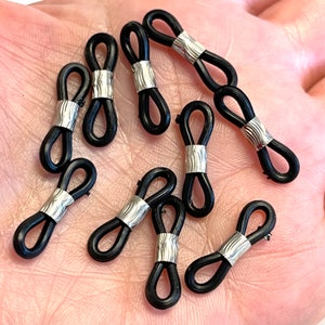 以下が含まれることがあります： 銀色の金属製のアクセントが付いた、黒いゴム製の眼鏡ホルダー10個のクローズアップ。ホルダーは8の字形です。