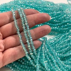 May include: A strand of turquoise blue crystal beads with a faceted finish. The beads are small and uniform in size, creating a delicate and elegant look.