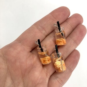 Peut inclure: Trois petits pots en verre remplis de tranches d'orange et d'eau, chacun avec une paille noire et une boucle de fil argenté en haut.