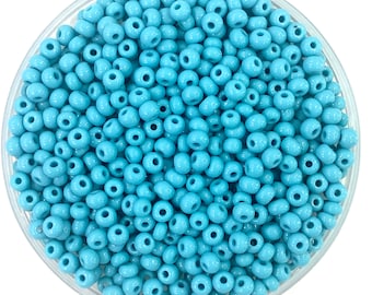 Puede incluir: Una vista cercana de un tazón lleno de cuentas de semillas de color azul claro. Las cuentas son pequeñas y redondas, y están dispuestas en un patrón aleatorio.