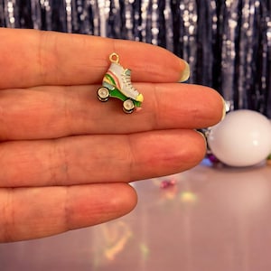 May include: A miniature roller skate charm with a gold loop. The skate has a white boot with rainbow stripes, green and yellow details, and black wheels. Ideal for jewellery making or adding to a keyring. The charm is approximately 2 cm in length.
