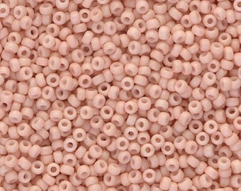 May include: A close-up image of a large quantity of small, round, light pink beads. The beads are all the same size and shape, and they are arranged in a random pattern.