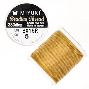 Op de afbeelding: Een spoel Miyuki Beading Thread in goudkleur, 330dtex, 100% nylon, gemaakt in Japan. Het label vermeldt "LOT. BX15R COL. 5".