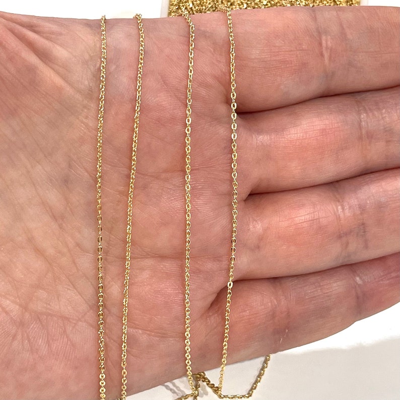 May include: Four strands of gold chain, varying in length, are displayed on a hand. The chains are delicate and have a fine, uniform link pattern.