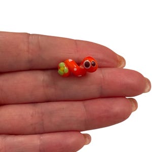 Pode incluir: Um pequeno verme de cerâmica pintado à mão, de cor laranja e branca, com olhos pretos e detalhes de flores verdes.