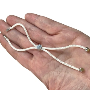 Puede incluir: Pulsera de cuerda blanca con una cuenta plateada y dos cuentas doradas.