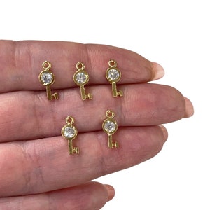 May include: Five gold key charms with clear rhinestone accents. The charms are small and delicate, perfect for adding a touch of sparkle to jewellery or crafts.