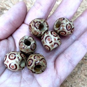 May include: Six wooden beads with a geometric pattern in shades of brown and red. The beads have a hole in the centre for threading.