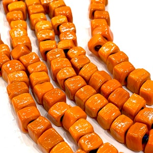 May include: A strand of orange and brown ceramic beads, each bead is square shaped and has a textured surface.