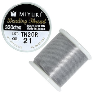 Pode incluir: Uma bobina de fio para miçangas Miyuki de cor cinza prateado, 330dtex, 100% nylon, feito no Japão. O rótulo diz "LOT. TN2OR COL. 21".