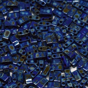 May include: A close-up of a pile of small, blue and brown rectangular glass beads. The beads have a metallic sheen and are perfect for jewelry making.