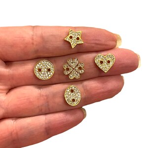 May include: Five gold-toned metal charms with clear rhinestone embellishments. The charms are shaped like a star, heart, clover, and two different sized circles.