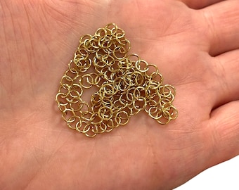 May include: A pile of gold jump rings, a type of jewelry finding, on a hand.