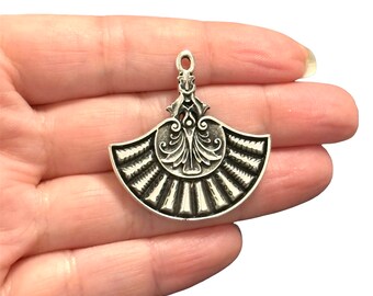 May include: Silver-toned metal pendant charm in the shape of a fan with an ornate design. The fan is open and has a detailed floral pattern in the center.