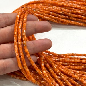 May include: A strand of orange and white shell beads. The beads are square shaped and have a glossy finish.
