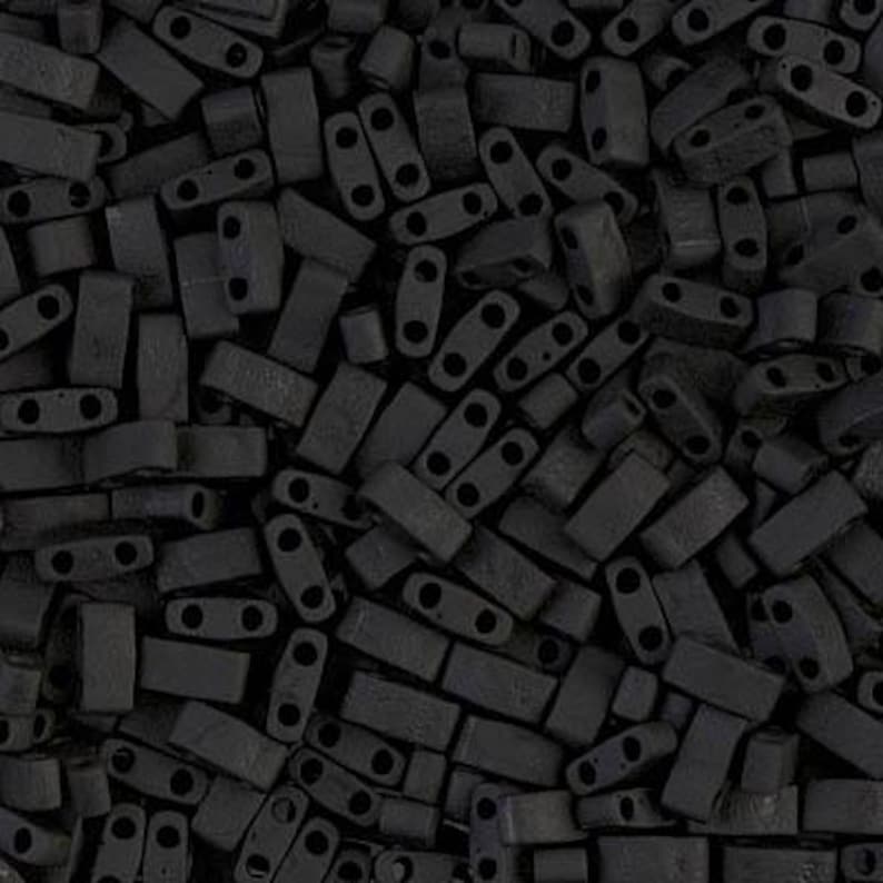 May include: A close-up image of a large pile of black rectangular beads with two holes in each bead. The beads are made of a matte material and have a slightly textured surface.