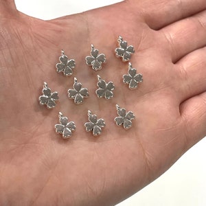 May include: A collection of silver-toned metal charms shaped like four-leaf clovers. The charms are small and delicate, perfect for adding a touch of whimsy to jewellery or crafts.